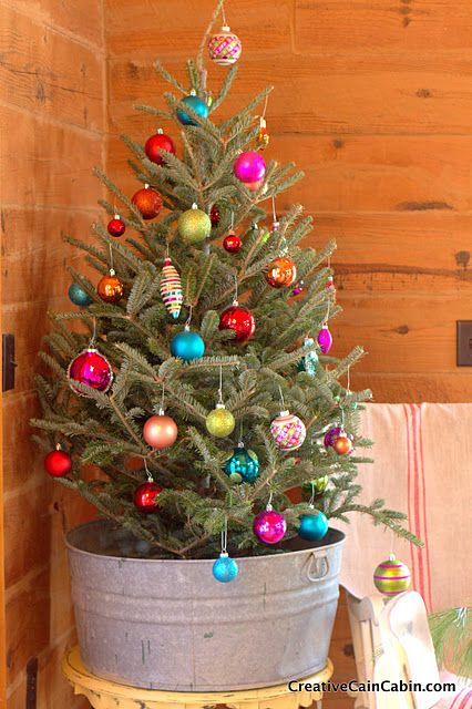 A galvanized bucket with a small tree in it and colourful ornaments.