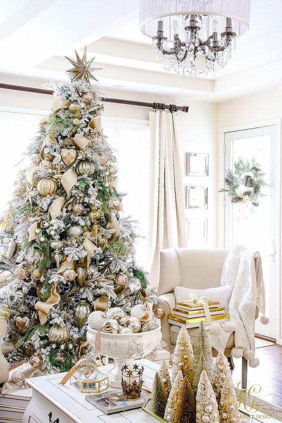 A large flocked Christmas tree is in the living room with gold accents.