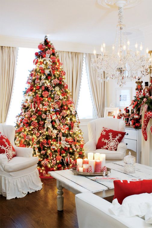 A classic red Christmas tree in the living room with a chandelier beside it.