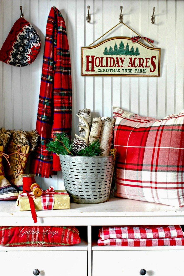 A plaid throw pillow on a wooden bench with a Holiday Acres sign above it.