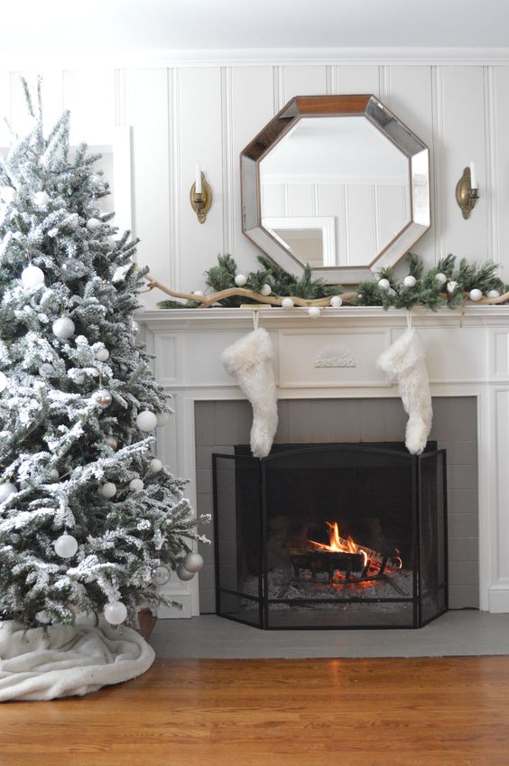 A white fireplace mantel with a tree beside it and white stockings hanging on the fireplace.