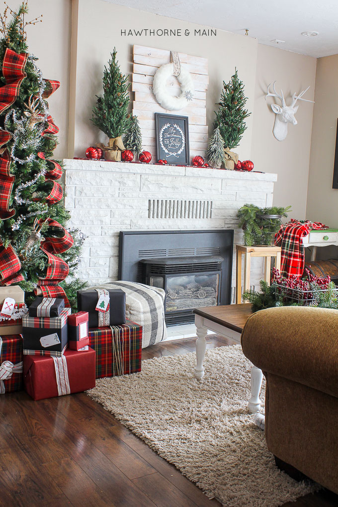 A white washed holiday fireplace mantel with small Christmas trees on it.