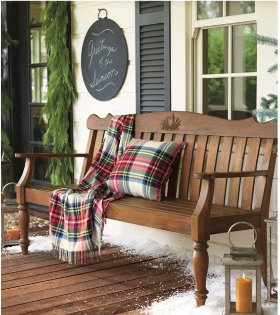 An outdoor wooden bench with a plaid throw pillow and blanket on it.