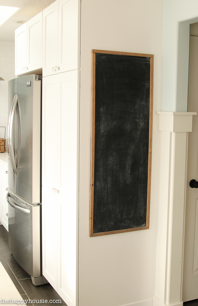The chalkboard on a wall beside the kitchen cabinets.