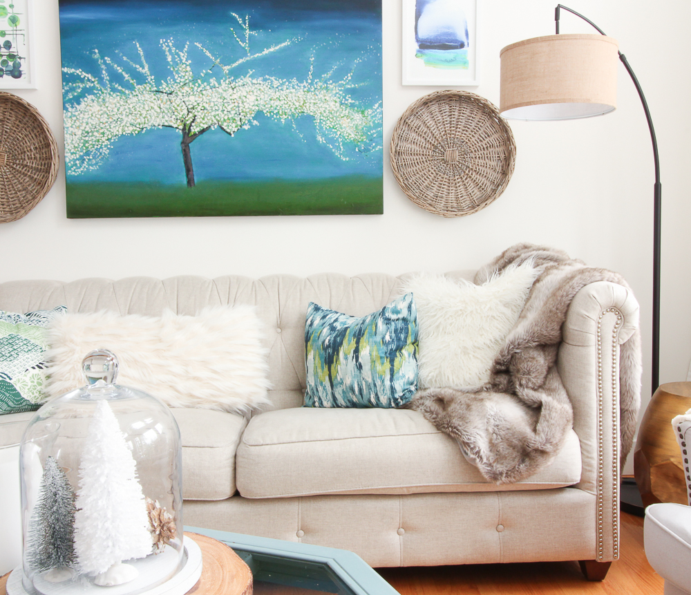 A bright blue painting is above the neutral couch on the wall.
