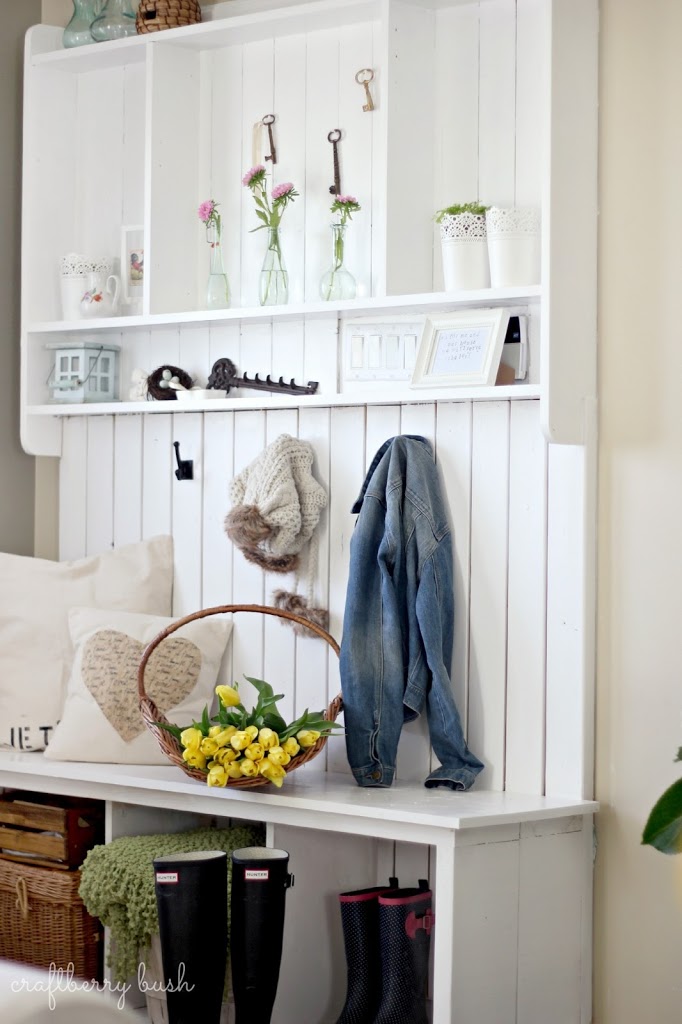 A white mudroom built in closet with a basket filled with yellow flowers on the bench.