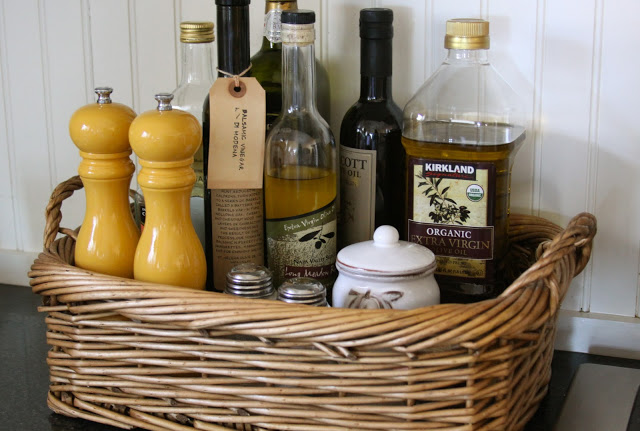 Vinegars and oils in a basket on the kitchen counter.