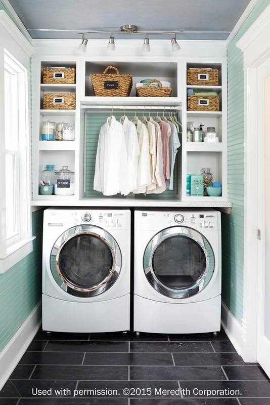 A small laundry room with shirts for ironing hanging above the washer and dryer.