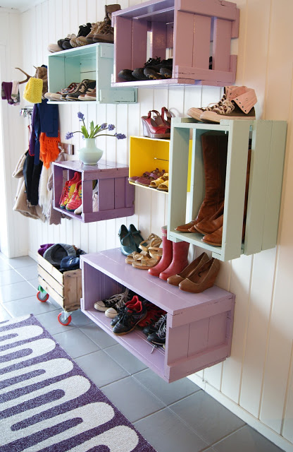 Wooden crates painted pastel colours nailed to the wall with boots and shoes in them.