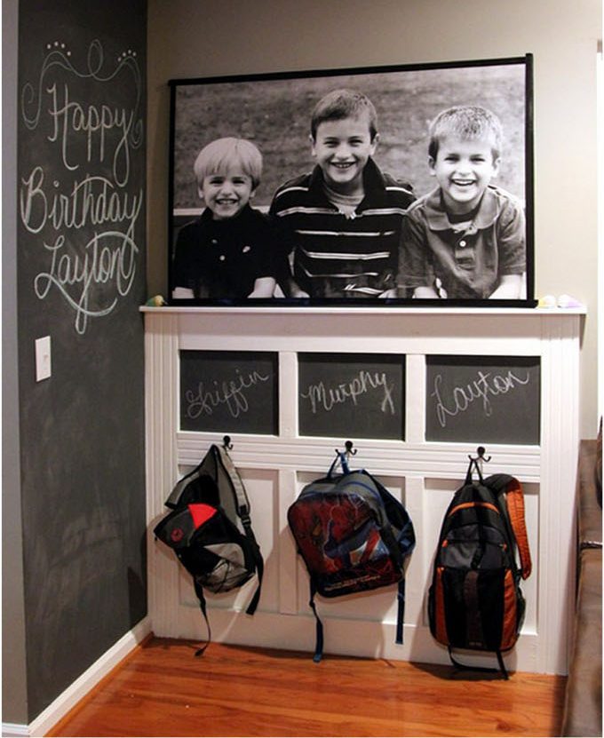 Backpacks on the wall with a picture of the 3 children above them.