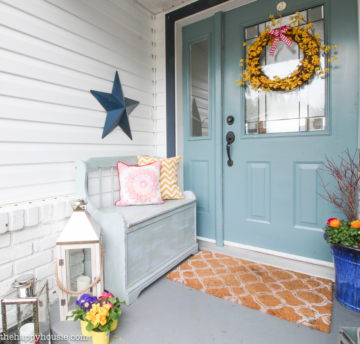 A small grey bench with throw pillows is by the front door.