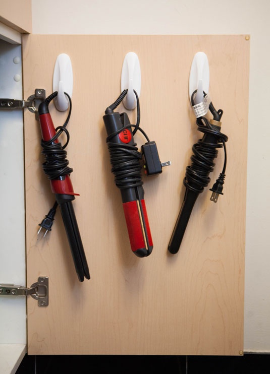 Hooks on the back of a cabinet door with curling irons and flat irons hanging on them.