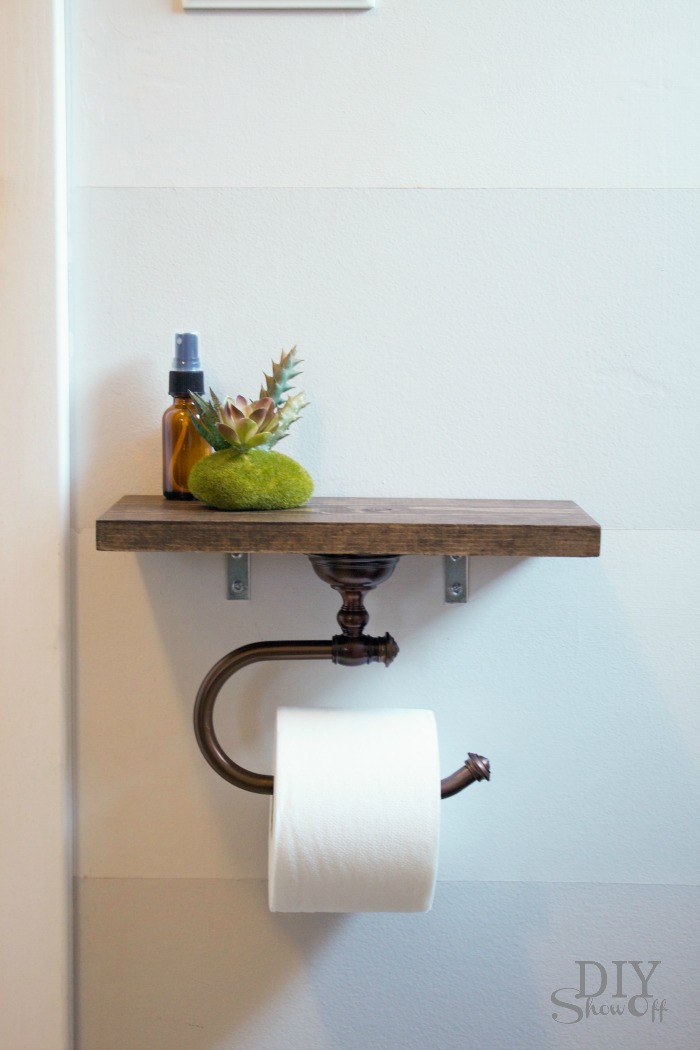 A small wooden shelf that holds bathroom products on top and and a toilet paper holder on the bottom.
