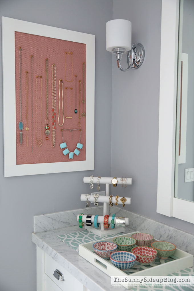 A jewellery cabinet filled with necklaces on the bathroom wall.