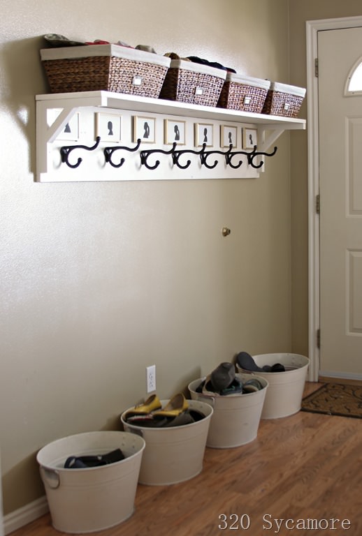 Buckets underneath hallway entryway hooks for jackets with shoes inside of them.