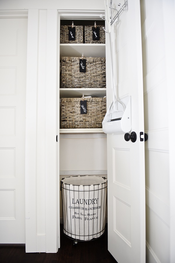 Neutral linen closet with a small laundry basket in the bottom of it.
