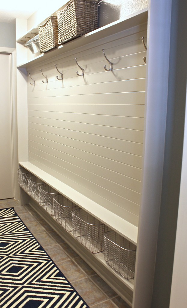 A white wall with hooks, wicker baskets and metal wire baskets in the mud room.