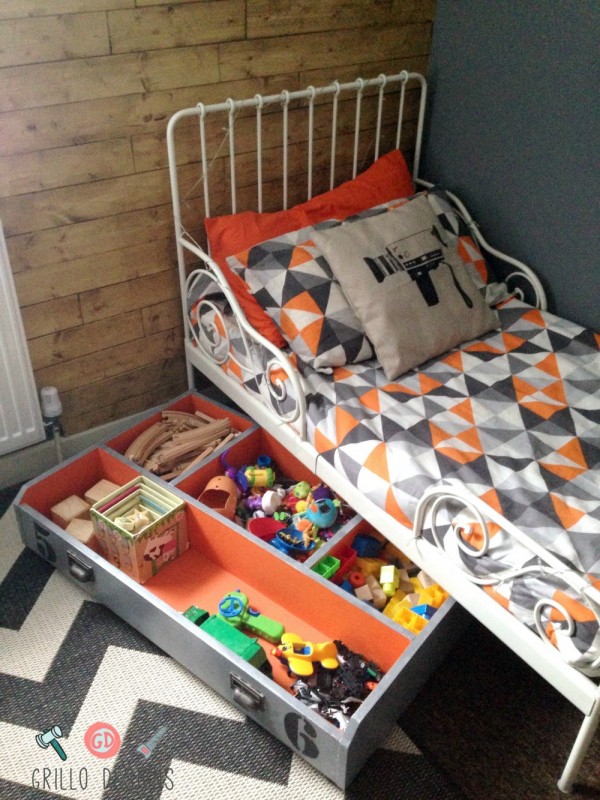 A small wire framed bed with a drawer filled with toys.