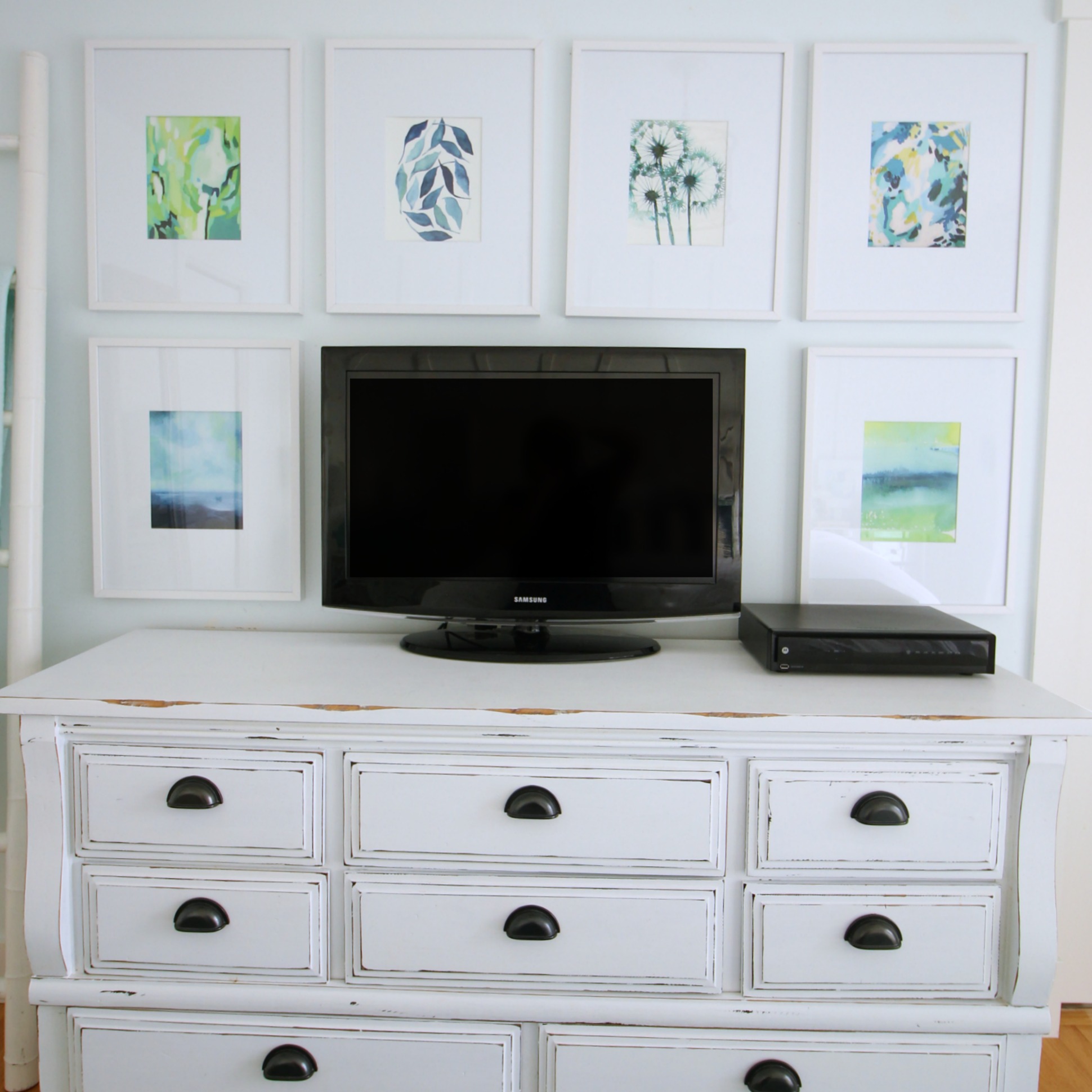 A gallery wall above a white dresser with a TV on it.