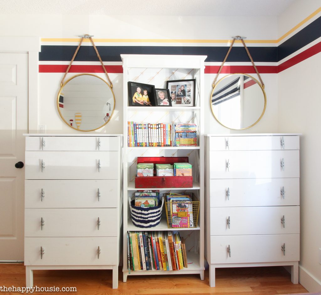 Two dressers with a bookshelf in the middle an two mirrors.