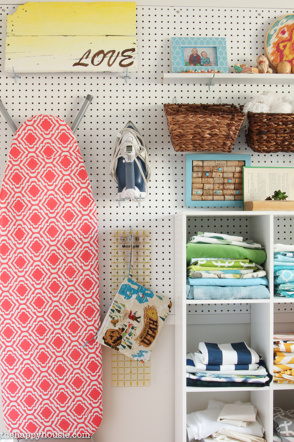 A peg board wall with an ironing board, iron hanging on it.
