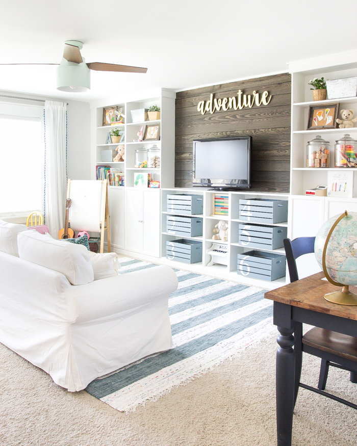 A shelving unit in a rec room that has wooden baskets and shelves with decor items.