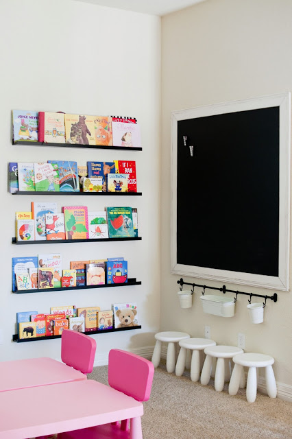 A playroom with a blackboard and a small desk with pink chairs.