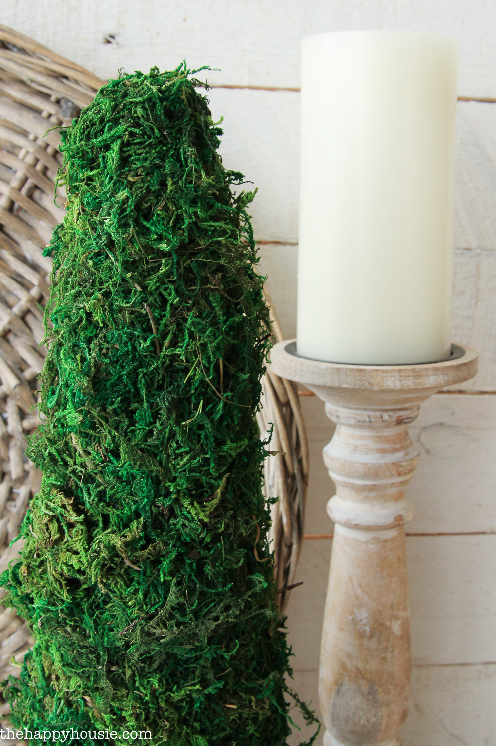 A candlestick and white candle beside the topiary.