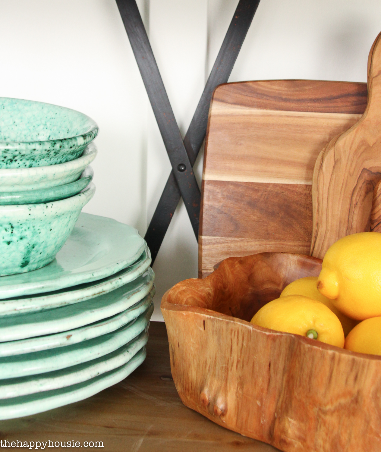 Soft green dishes are on the open shelving unit beside the lemons.