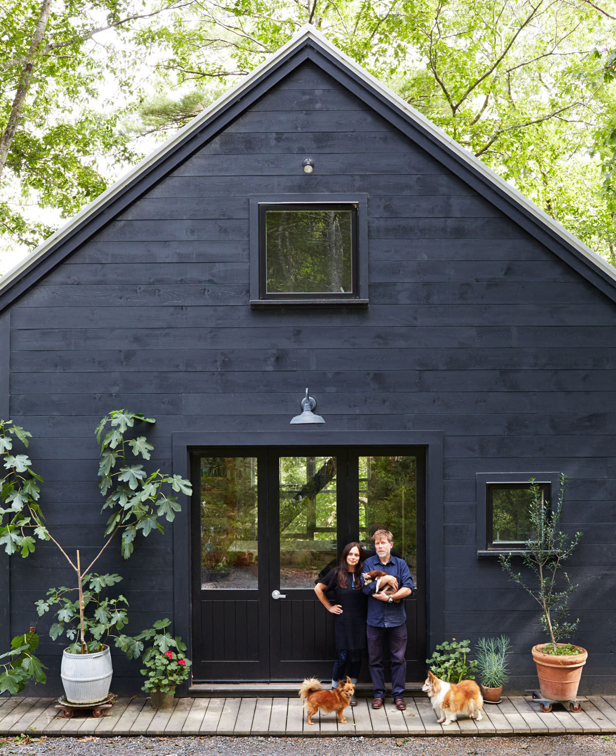 A very dark navy with black trimmed house and two people and their dogs on the deck.