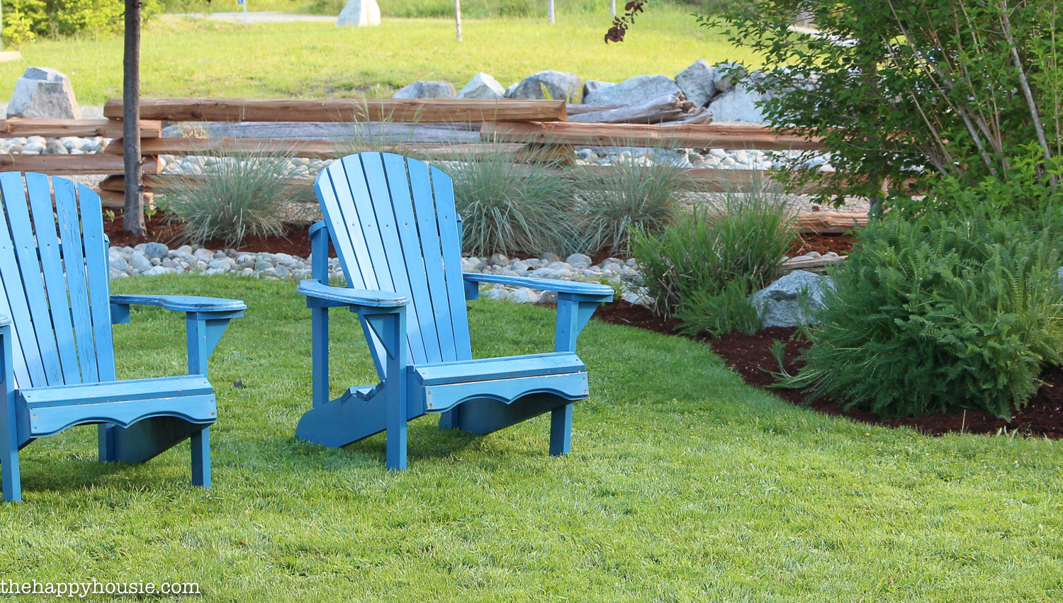 Two blue Adirondack chairs on the lawn of the house.