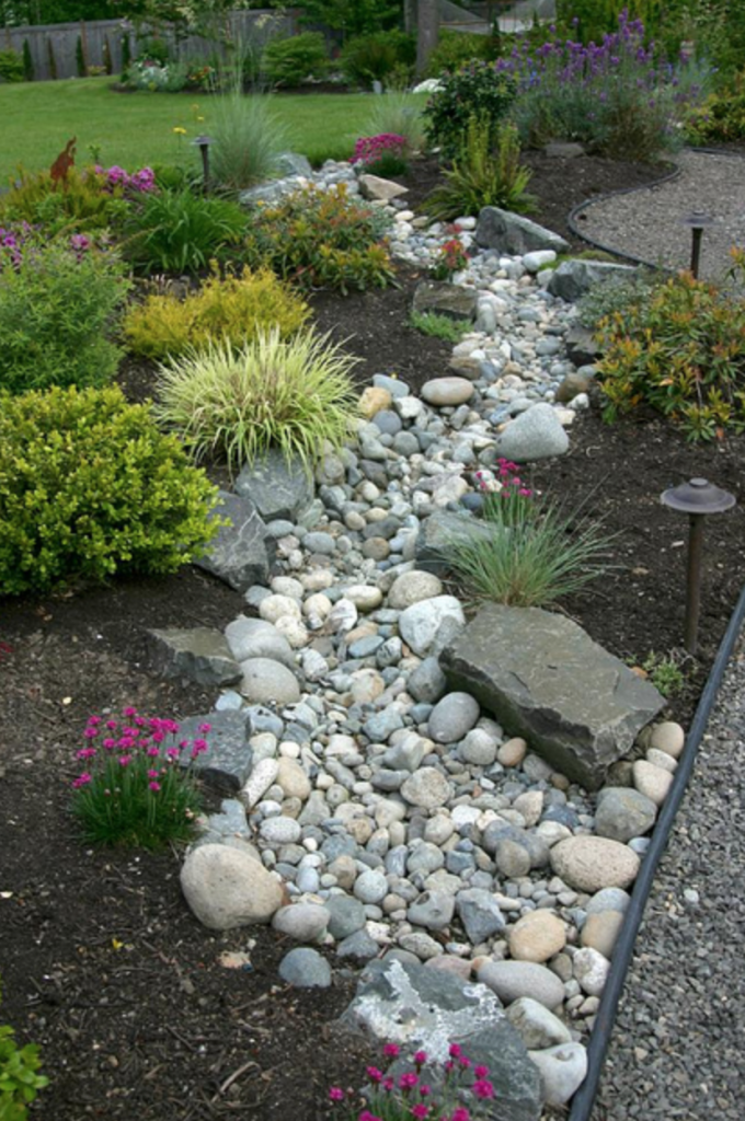A large traditional garden with river rock winding through the flowers and bushes.