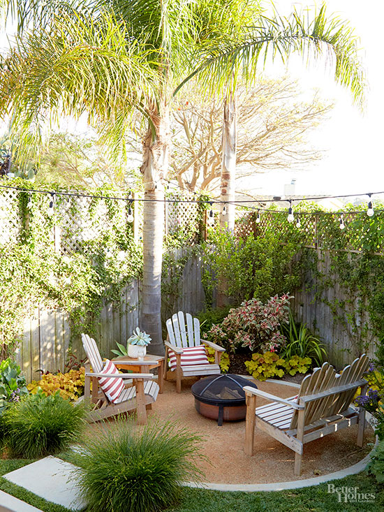 A small corner of a yard with a fire pit and chairs around it, plus a large tree beside the area.