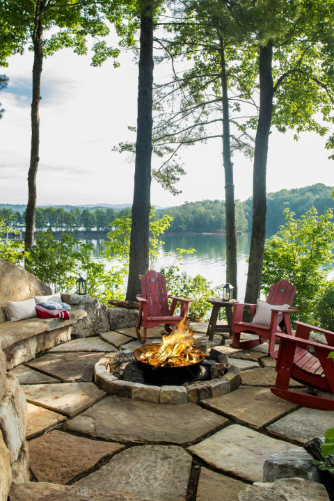 A lakeside fire pit with red chairs.