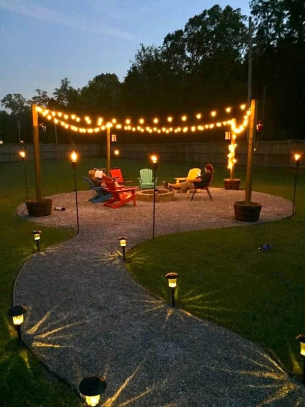 A small patio in the center of a yard with lights and chairs.