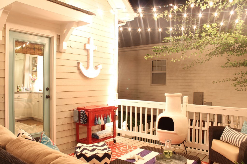 A little deck with an anchor hanging on the outside wall and lights strung up.