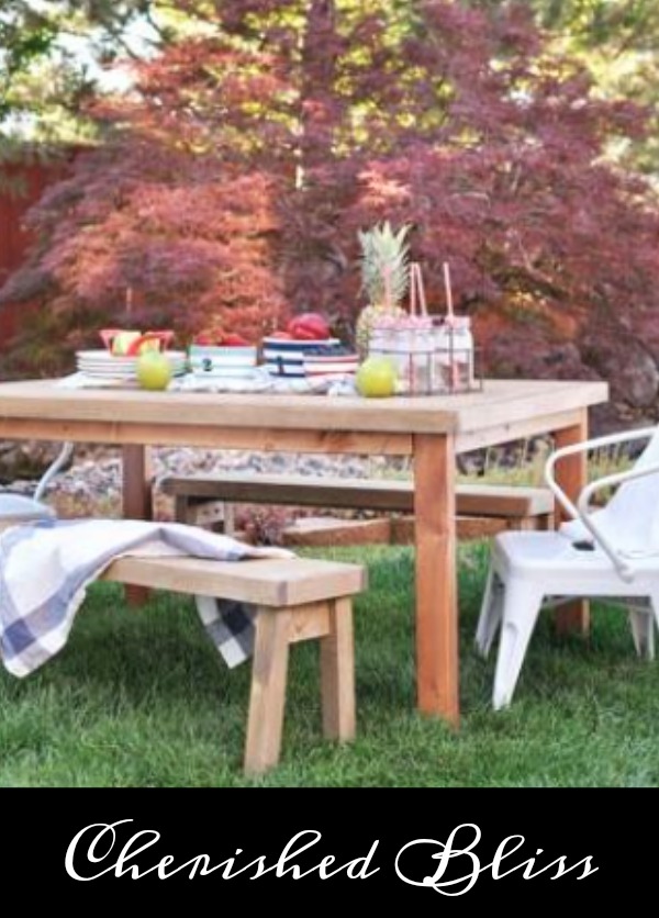 An outdoor picnic table set for a meal with a checkered blanket on the bench seat.