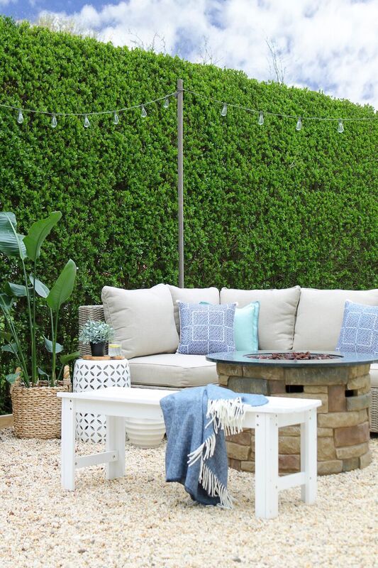 A large green hedge with a small couch and white table on the patio.
