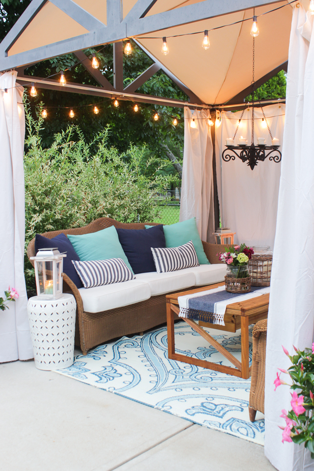 A small chandelier and patio lights underneath a gazebo with a couch and table.