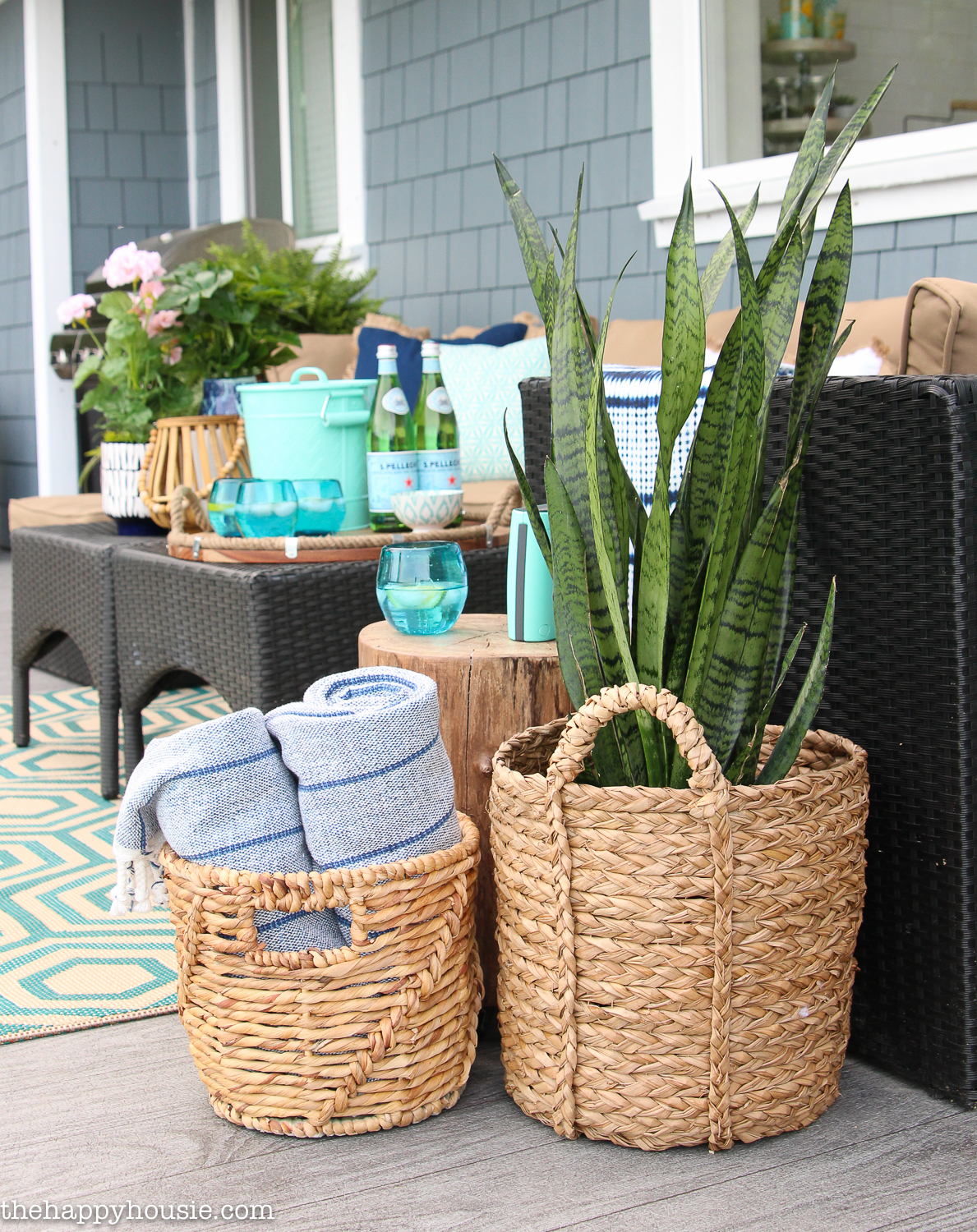 Large wicker baskets on the porch with a plant in one and rolled up blankets in another.
