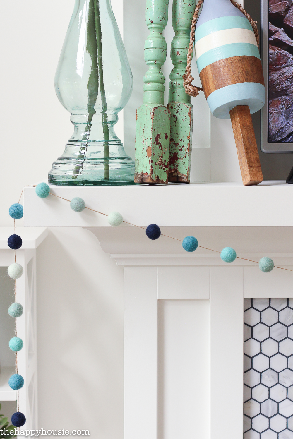 A white fireplace mantel with the garland hanging in front of it.