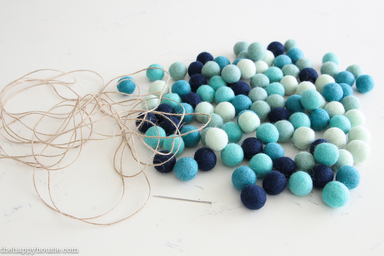 Light blue, dark blue and white felt balls on the counter with a needle and thread.