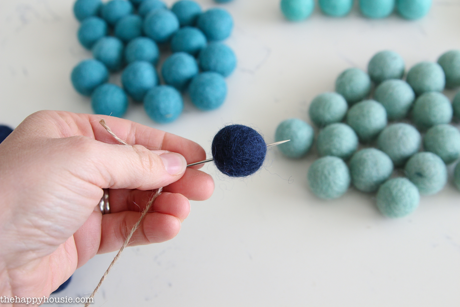 One of the felt balls being threaded onto the string with a needle.