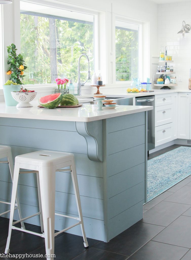 A pastel blue island with white stools.