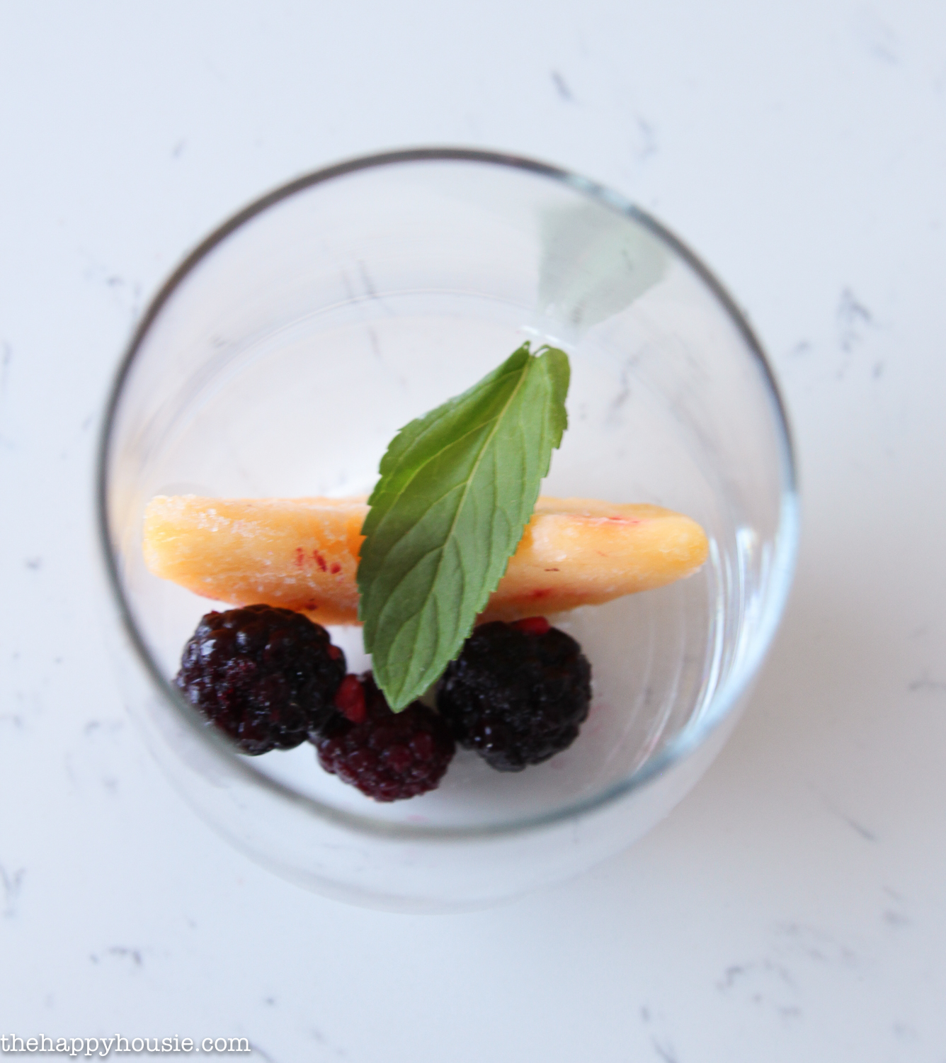 Balckberries, peaches, and a mint leaf in a glass.