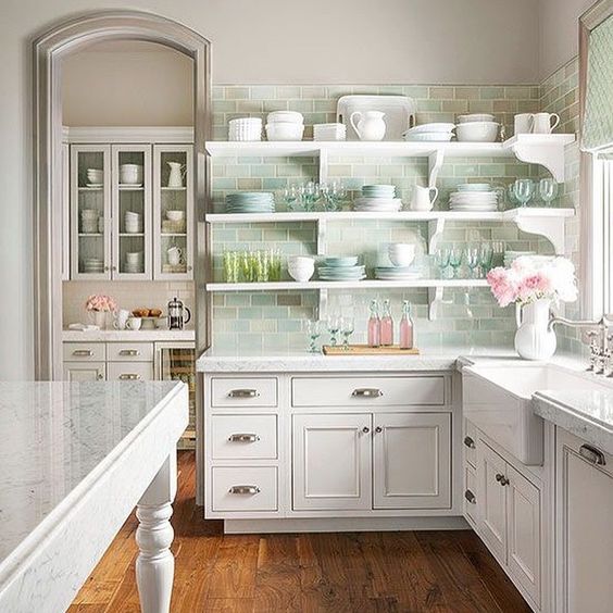 White cabinetry and open shelves with pink and green glass in the kitchen.