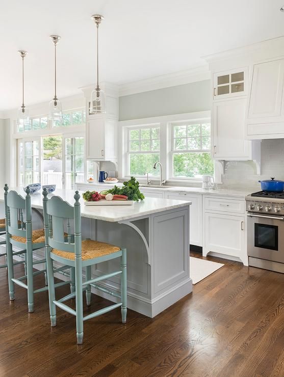 A white kitchen with a grey/blue island and light blue chairs.