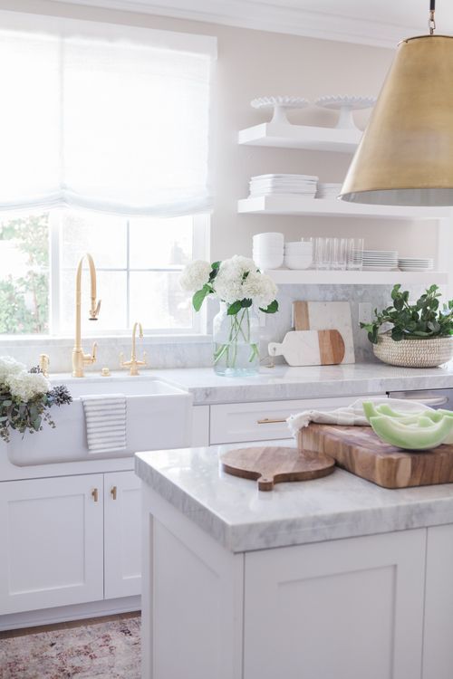 A white kitchen with brass faucet and white open shelves.