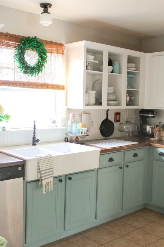 A farmhouse sink, light blue cabinets and a green wreath in the kitchen.
