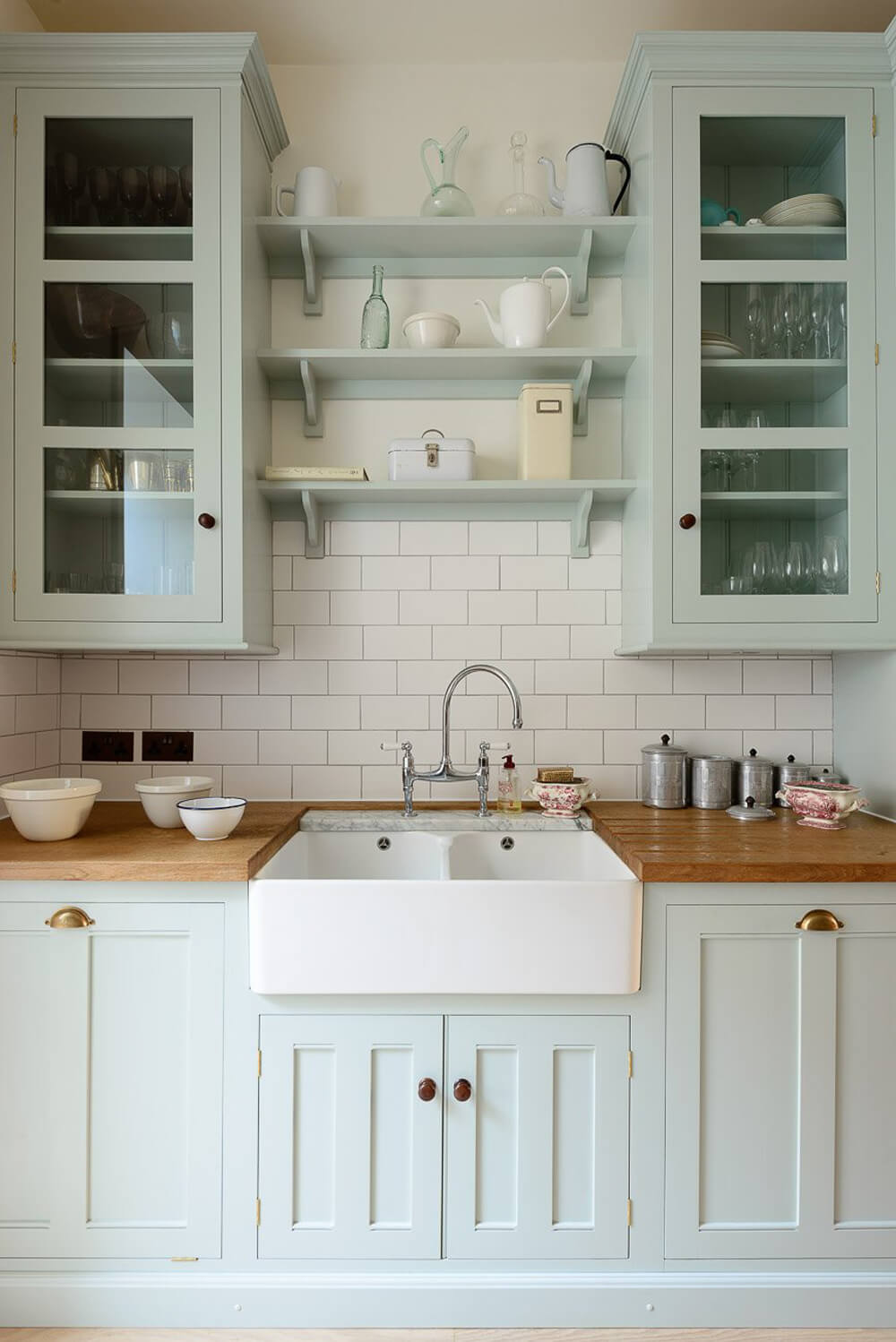 Mint green cabinets in the kitchen with a white backsplash and a wooden counter.